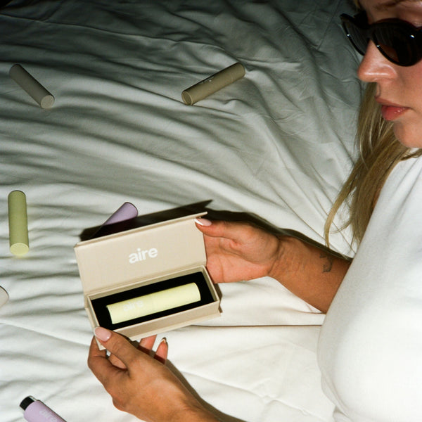 Person holding a mouth spray on a bed with various mouth spray products around aesthetically.